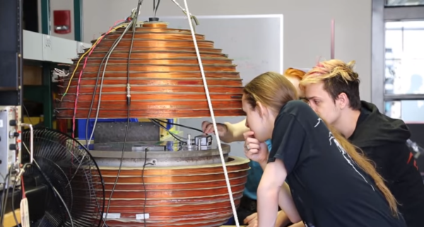 Several MIT students peering into a spherical apparatus with various wires attached.