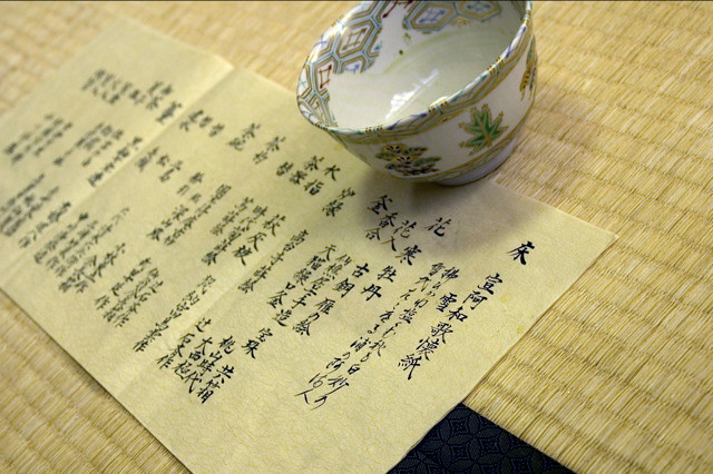 A cup and a piece of paper with hand-written Japanese kanji characters on it
